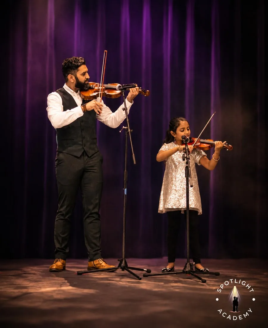 Adult and child violin students performing together on a spotlit stage at Spotlight Academy, The Woodlands TX